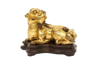 Lot 208 - A CHINESE GILT-BRONZE FIGURE OF A MYTHICAL BEAST WITH WOOD STAND